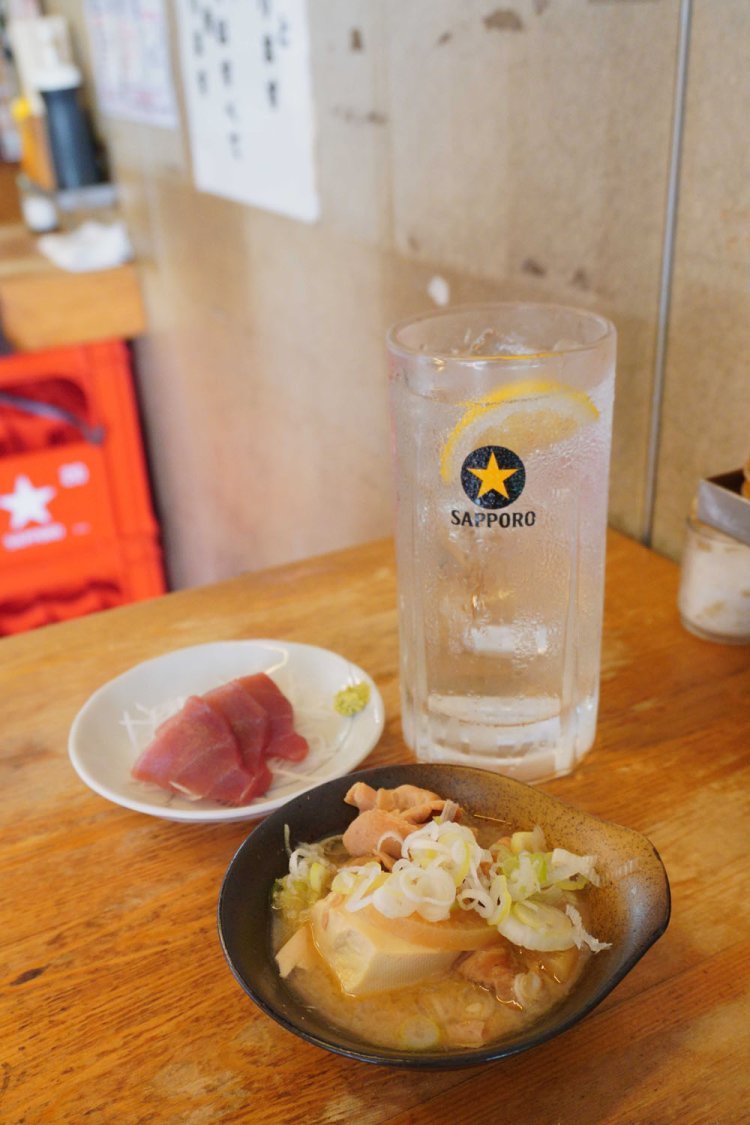 煮込み150円（前）、マグロ刺し180円（奥）、酎ハイ250円。3品で580円という安さだ。