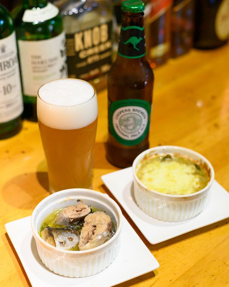 オーストラリアのクーパーズエール700円。酒肴は、さばガーリックアヒージョ600円（左）など、缶詰料理が中心。