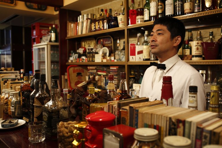 白いバーコートと蝶ネクタイ姿でカウンターに立つオーナー・間口一就さん。