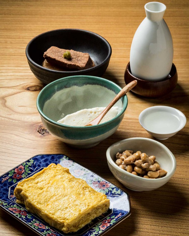 手前から出汁巻き玉子、自家製納豆と豆腐、牛肉と大根のバーボン煮。ぬる燗は喜久醉（静岡）。