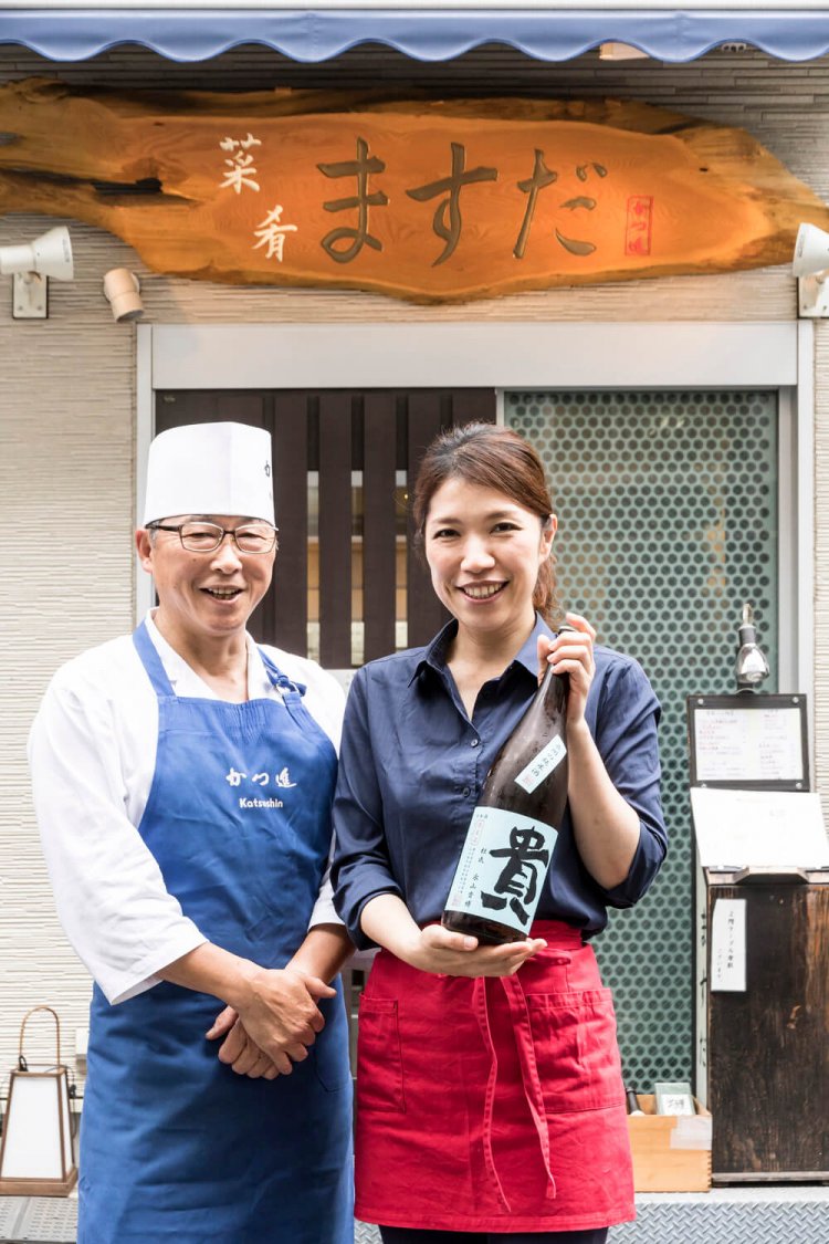 坪さん（左）と増田さん（右）。看板の字は増田さんのもの。