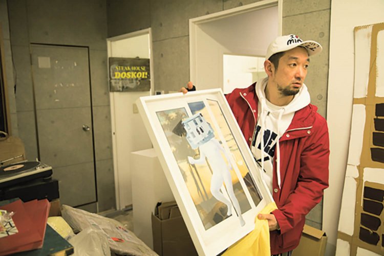 自作品を手にするCOBRAさん。後方にミニギャラリー「THE STEAK HOU SE DOSKOI」が。