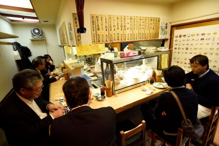 カウンターは常連でぎっしり。通路挟みテーブル席も。