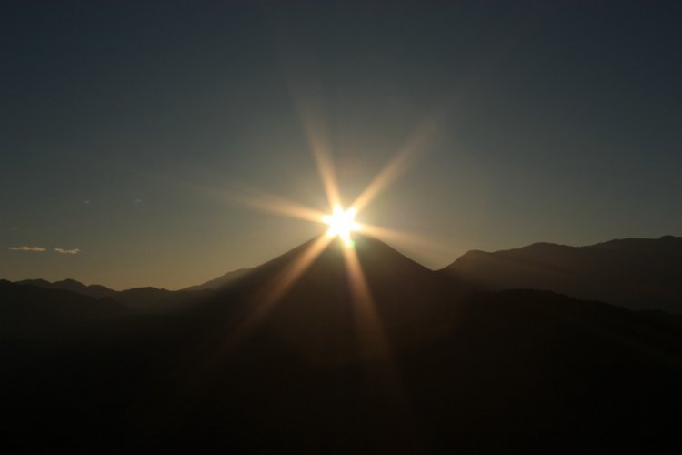 富士山の山頂と昇る朝日が重なる幻想的な光景。