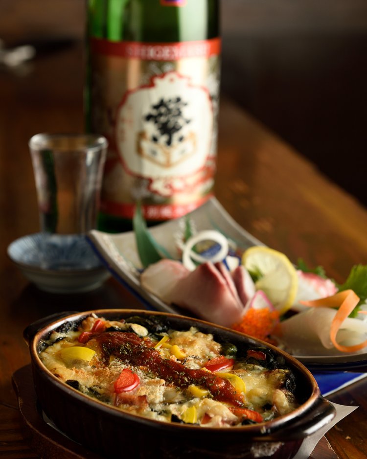 有頭エビのソースがかかるカキとちぢみほうれん草のグラタン824円、ブリ、真鯛などが彩る刺身のおまかせ3点盛り1058円。地酒は各734 円。