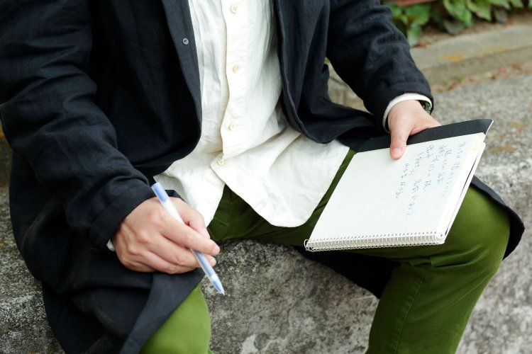 小雨が降る桜橋のたもとにて。「見たものや誰かがすれ違い様に言ったことをメモします。普段はスマホに記録することも」。