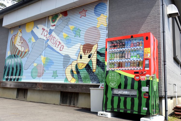 境内の公民館横に置かれたスイカ柄の自販機と中学生のスイカ画。