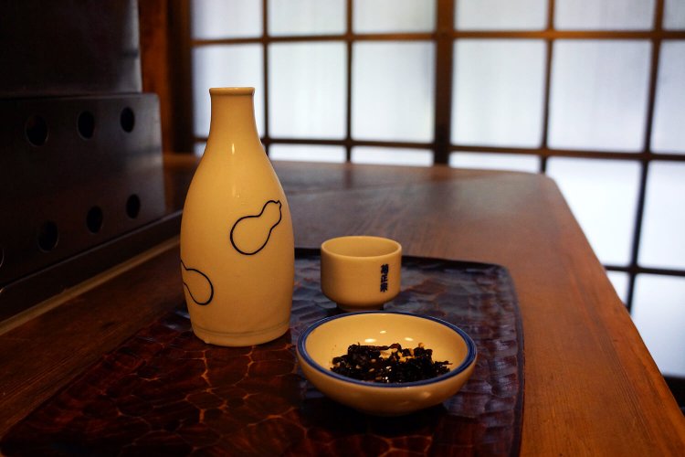 お通しの昆布の佃煮とともにお盆に。これがカウンター席の基本スタイル。菊正宗樽酒は一合700円。