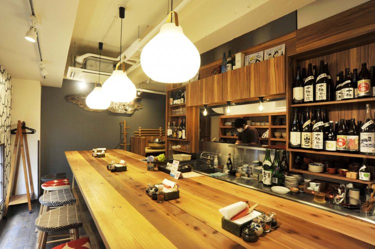 大きな白木のテーブルが置かれた店内は、小粋な料理屋といった雰囲気。棚には神奈川の地酒が並ぶ。