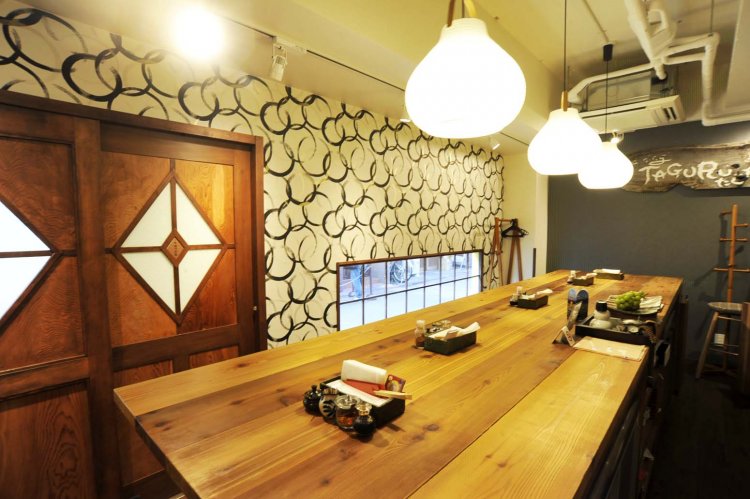 大きな白木のテーブルが置かれた店内は、小粋な料理屋といった雰囲気。棚に神奈川県産の地酒が並ぶ。