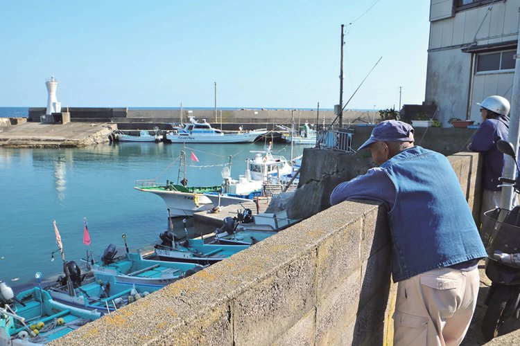 漁港を眺めている御高齢の漁師。夕方の出航前の、のんびりした時間を過ごしている。 