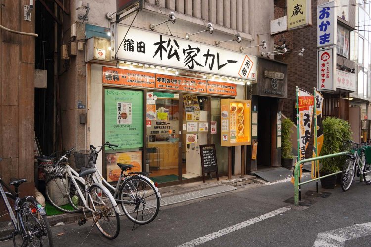 「学割あります」「ライス大盛無料」などの文字が目立つ店頭。「マンガ新入荷情報」の黒板も置かれている。