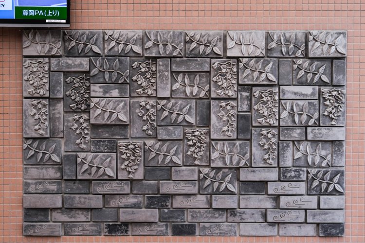 市の花・フジを全面にあしらったこの作品もれっきとした“鬼瓦”だ（ららん藤岡内トイレ壁面）。