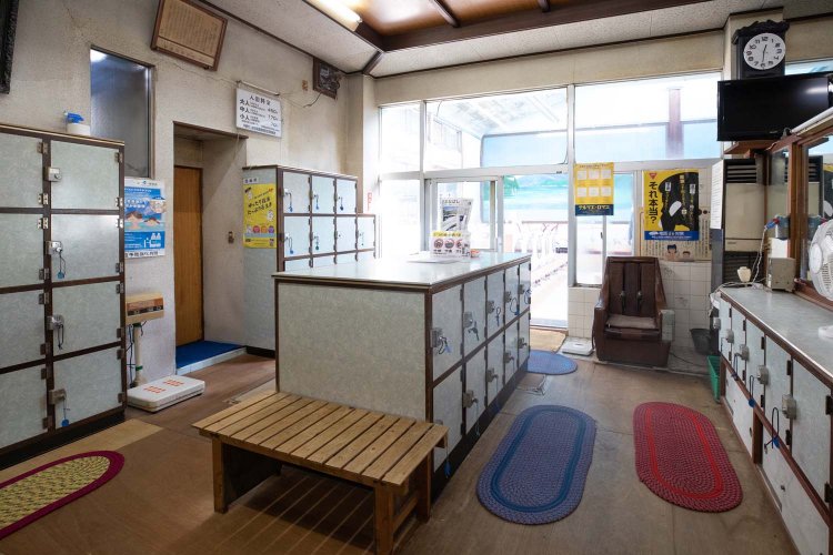 男湯の脱衣所。板張りの床に木のベンチ。浴室側に置かれたマッサージチェアが渋い。