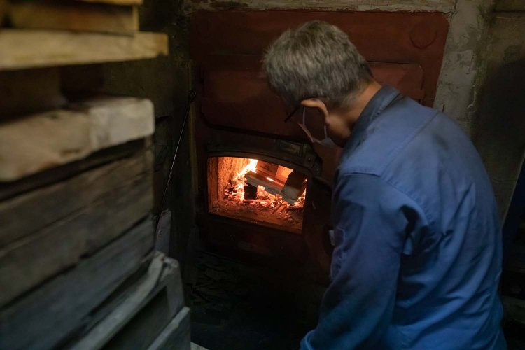 裏のボイラー室で釜に薪をくべる松柳さん。職人技だ。