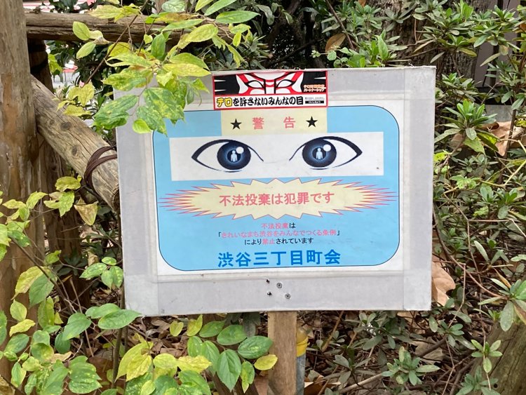 渋谷の植え込みにあった立て札。目のイラストと隈取ステッカーの合わせ技である（渋谷・2020年）