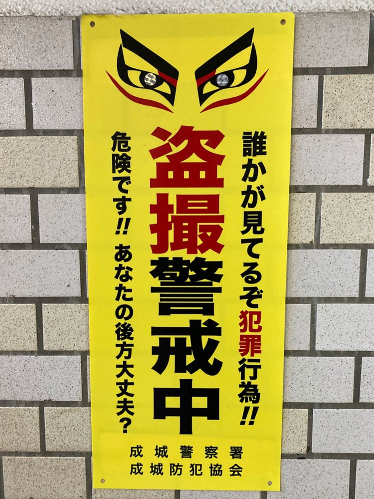 駅に貼られた盗撮禁止プレート。目玉の部分が反射素材になっている（千歳烏山・2020年）
