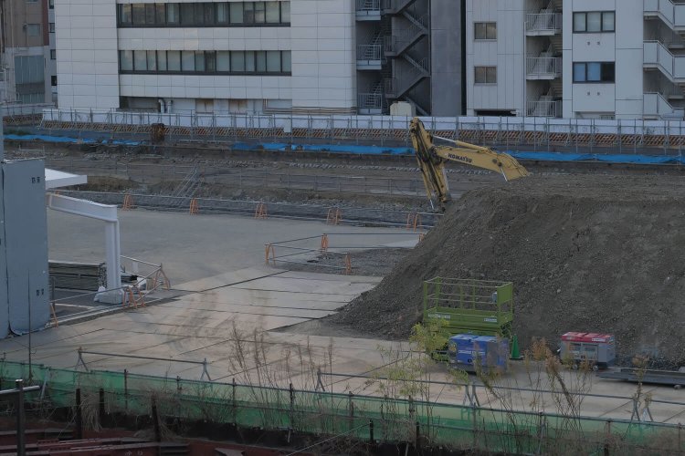 高輪ゲートウェイ駅改札外から“高輪築堤”をみる。ショベルカーのアーム部分にうっすらとグレー色の石垣が見えるはず……。2021年2月撮影。