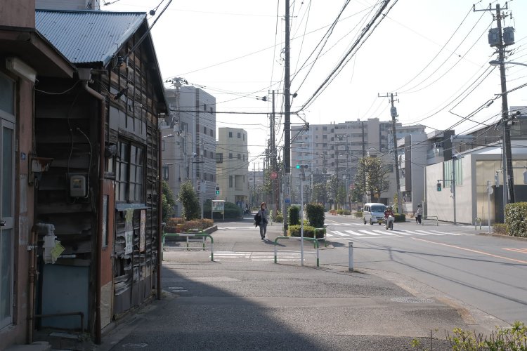 軽バンとスクーターが走る道路が須賀線の跡。左の古い家屋は鉄道があった時代を知っているのだろうか。