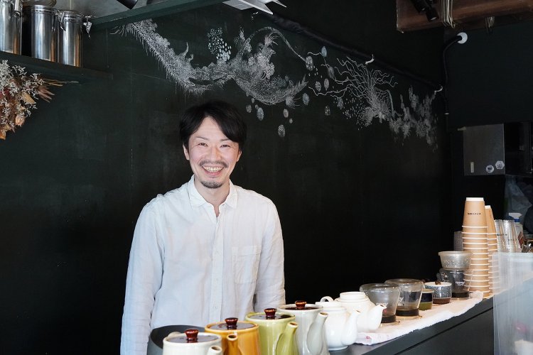 店主の高安さん。後ろの壁は黒板になっていて、知人にチョークで絵を描いてもらっている。