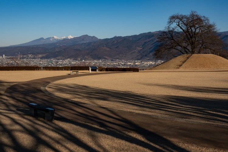 直径 23 ｍの盃塚古墳の先には八ヶ岳（左奥）が鎮座している。