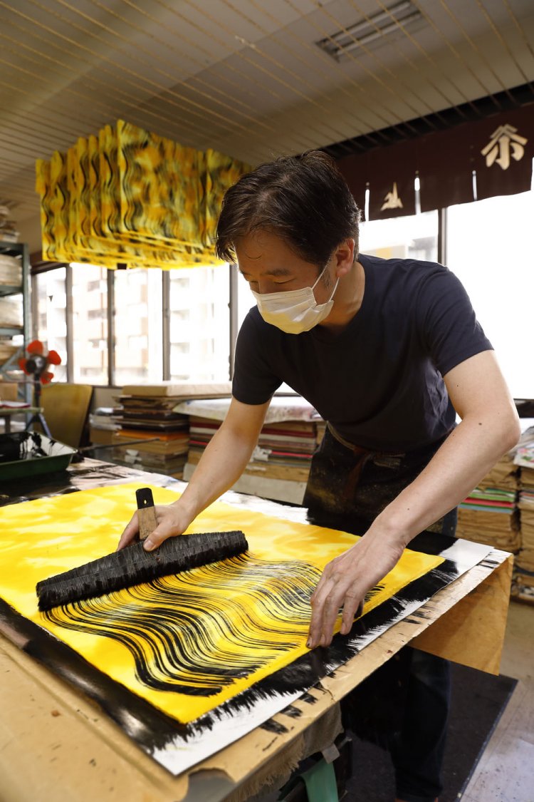 染め工房は見学可。写真は職人が下染めを済ませた和紙に刷毛で模様を描く場面。虎にちなんだデザインで、館内のショップでも販売される。