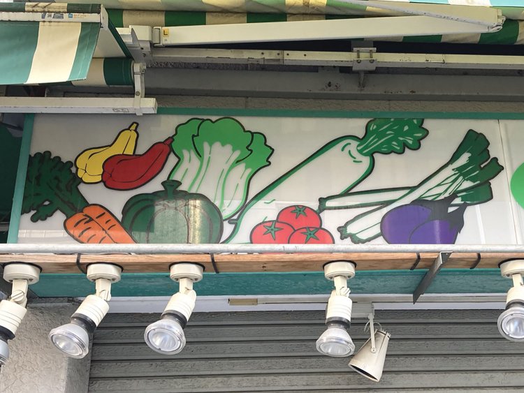 同じプラ看板の左と右に野菜と果物が勢ぞろい。全体的に迫力がある（2021年）。