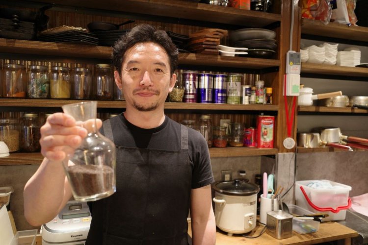 お気に入りのマスタードシードを手に持つ店主の小田さん。トークと気配りが上手な小田さんの人柄に惹かれて通う常連さんも多い。