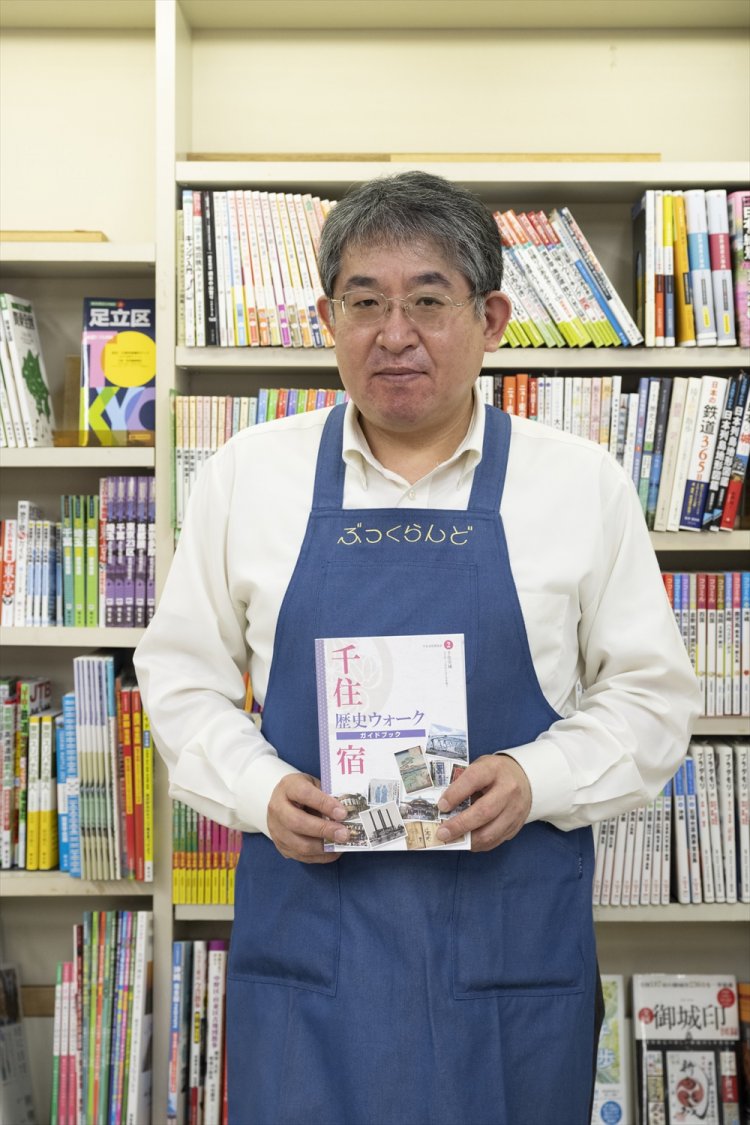 千住文化普及会発行『千住宿歴史ウォークガイドブック』を手にする佐々木副店長。「千住の人たちが作った名所旧跡ガイドは散歩に必携！」