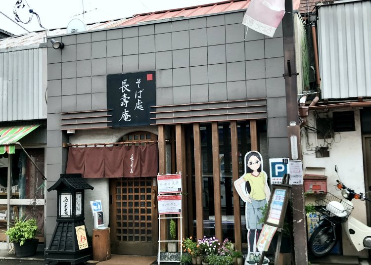 店舗向かって右に立つパネルは、飯能が舞台のアニメ『ヤマノススメ』のキャラクター。『長寿庵』もチラッと登場するらしい。