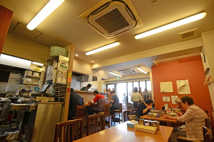 店内にはカウンター席とテーブル席があり、昼どきには空席待ちもできる。多くの客の前には支那そばの丼とカレーの皿が並んでいる。