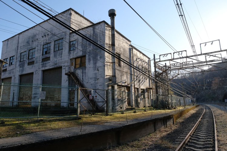 昭和12(1937)年築の変電所建屋は現役時の姿を色濃く残している。夕刻の斜光で新線下り線のレールが光る。