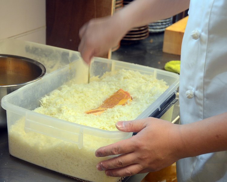 タッパーにたっぷりと入ったパン粉に肉をくぐらせる。最初はふんわりと衣付けした後にギュギュっと押し込むのが印象的。
