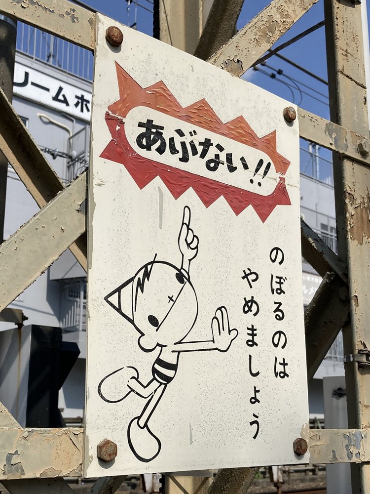 電車の送電鉄塔に掲示された看板。東京電力の旧キャラクター・ピカちゃんがあしらわれている（調布・2021年）