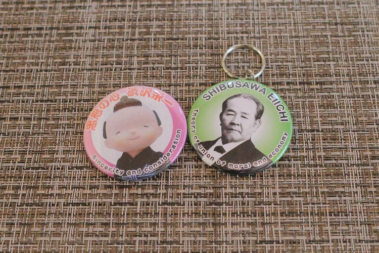 「栄一キーホルダー」（右、300円）は川本さんが最初につくったグッズ。