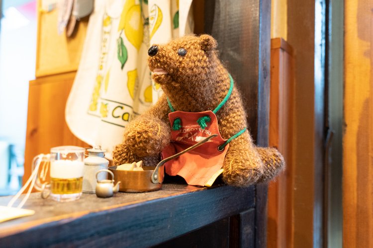 入り口脇にはクマのあみぐるみが、店のロゴマーク付きのエプロンをつけて座っている。