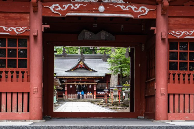 朱塗りで二層の楼門（御神門）から参道越しに社殿を望む。