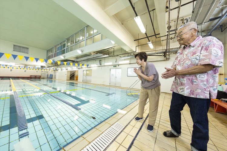 「あと5mでゴールですよ！　フレーフレー頑張ってー」クロールでターンして戻ってくる勇姿に声援を送る林さん夫妻。練習に励んだプールは当時と変わらない。