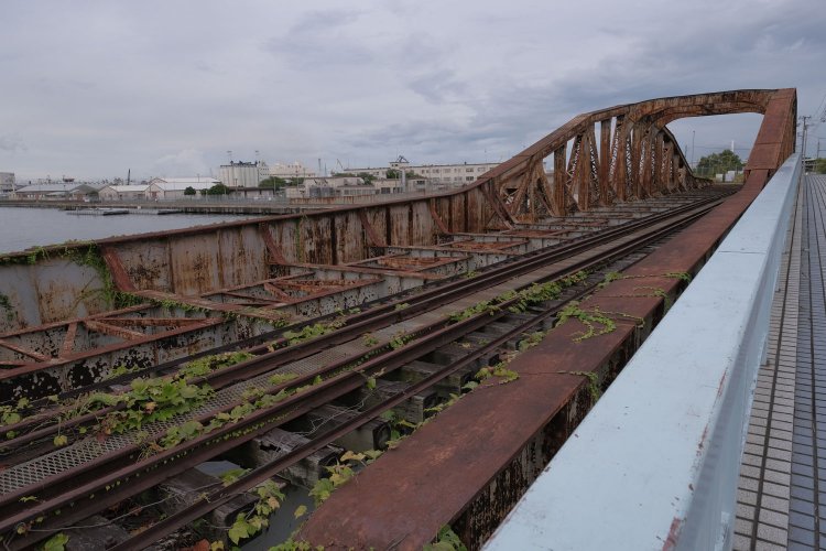 瑞穂橋のプレートガーダー部分。主桁は水平ではなく曲弦トラスへ向かってせり上がっている。レールはまだ敷かれたままである。背後は米軍基地。