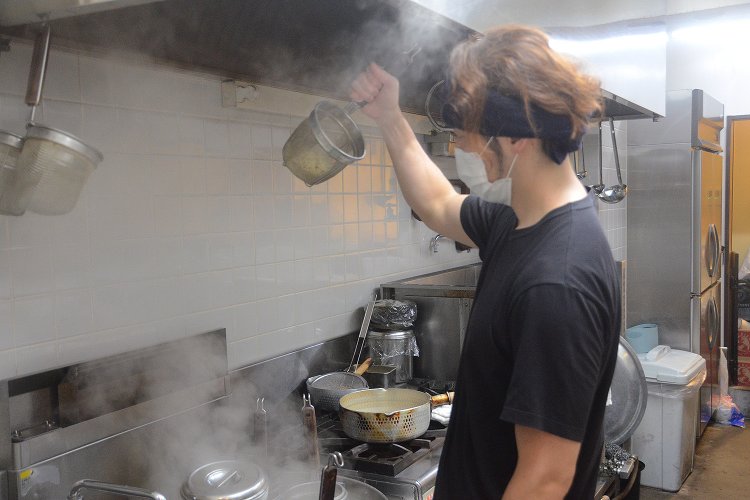麺の湯切りシーンを撮影。整理された厨房は「仕事ができる人はみんな持ち場をキレイにしていた」という西川さんの修業時代の体験に基づいている。