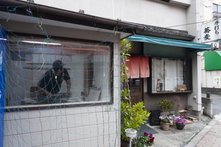 住宅地に突如現れる「手打ち蕎麦」の看板。外から窓越しにそばを打つ様子も見える。