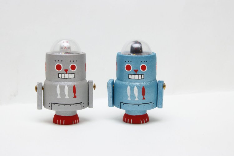 Ω（オーム）社さんのブリ木ガングネコロボット各4070円。高さ7㎝ほどの小さな木玩（木製玩具）のブリキロボット。頭上をよく見ると操縦席に招木猫（招き猫）が！