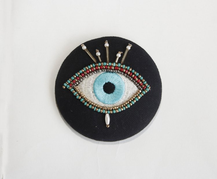 ポケットミラー1600円。ヨーロッパなどで魔除けとされる目を繊細なビーズ刺繍で描いた布製の携帯用ミラー。ベージュもあり。