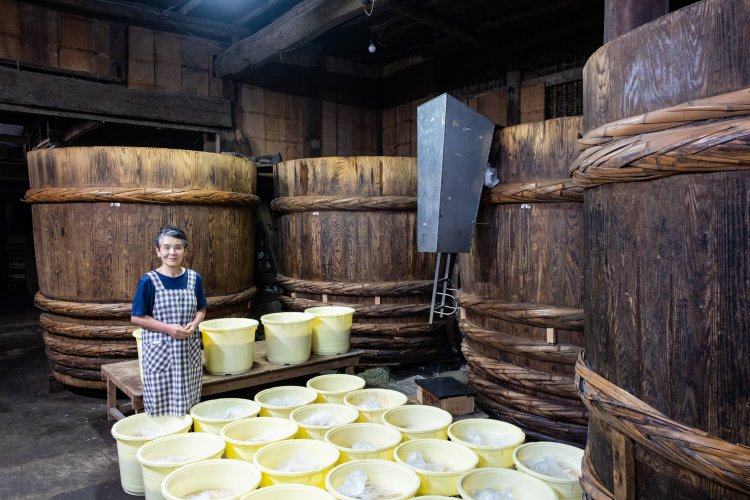 高さ約2ｍの杉樽が並ぶ味噌蔵と店を切り盛りする秋葉貞子さん。タイミングが合えば蔵見学もOKだ。