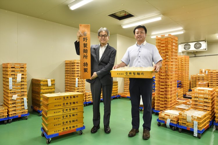 店の要望にがっちり応える。2代目社長の菅野善男さん（左）と営業部長の平賀貴博さん。冷蔵室には出荷前の麺がずらり。