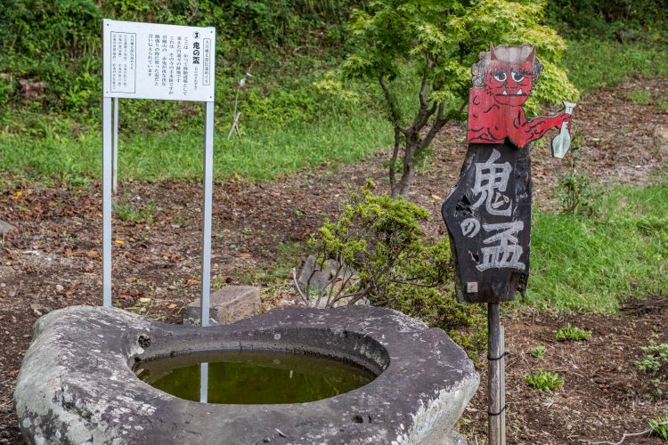 中央が窪んだ手水鉢（鬼の盃）。近くには桃太郎地蔵が立つ。
