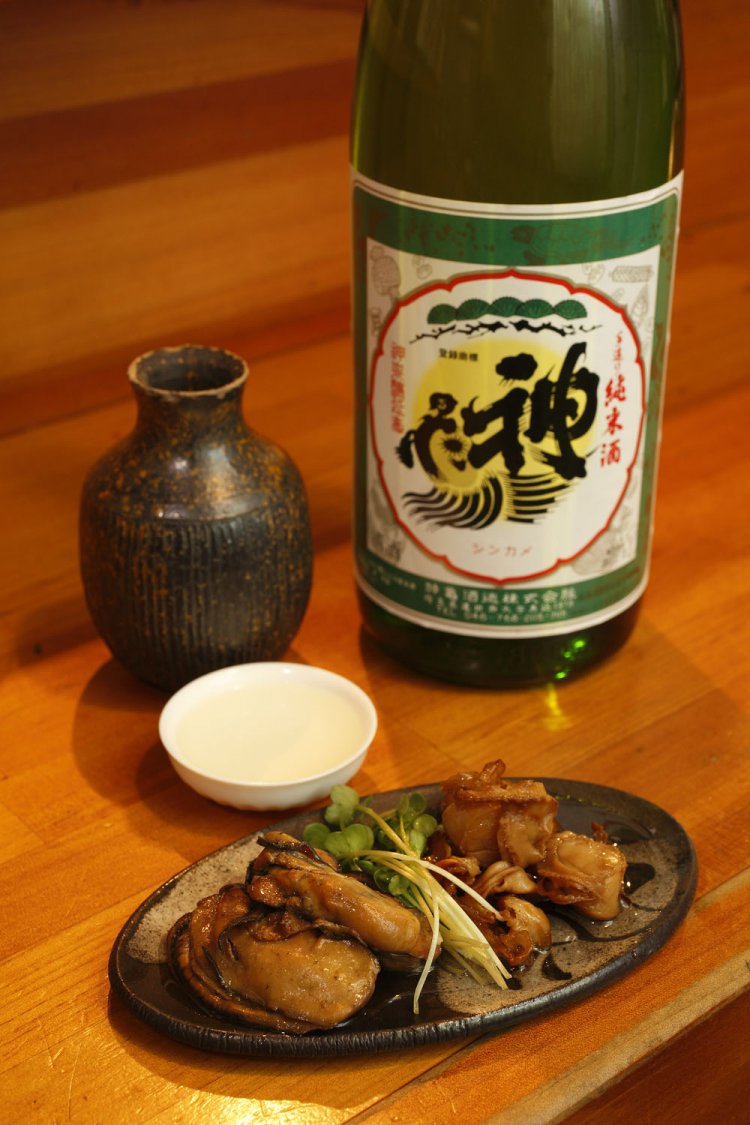 橋本家の癒やし酒でもあるという「神亀」純米甘口の酒800円（正一合）と牡蠣とホタテ貝燻製680円。「私が作るつまみをすべてつないでくれる酒です」。