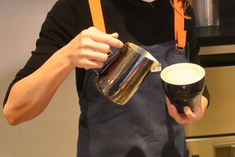 カフェラテにフォームミルクを注ぐバリスタ。