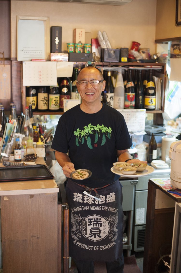 店主の石出博さん。ハーブやサラダで使うミニトマトは自家栽培。焼酎や泡盛などは80種類以上用意。もつ煮こみ440円も名物。