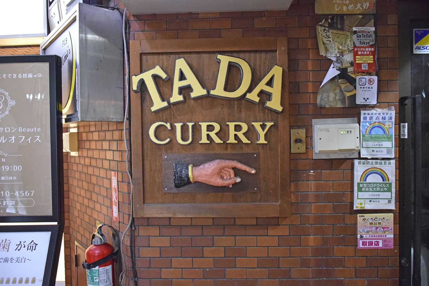 ビル入り口にある『TADA CURRY』の看板。手が指し示す先にお店のドアがある。
